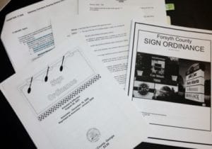 Documents related to Forsyth County sign ordinances and permits, provided by Pinnacle Custom Signs, showcasing various guidelines and regulations for obtaining sign permits. The image includes printed pages with detailed information and official stamps, essential for ensuring compliance with local signage laws.