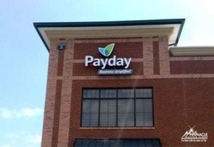 Exterior building sign for Payday, designed by Pinnacle Custom Signs, featuring the company’s logo and tagline 'Business simplified' in white and blue letters with a green leaf graphic. The sign is prominently displayed on a brick building, enhancing the business's visibility and branding.