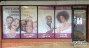 Engaging window graphics for a dental office, designed by Pinnacle Custom Signs, featuring images of smiling patients and text advertising services like extractions, root canals, and implants. The graphics cover multiple windows, improving the storefront's visibility and appeal to potential clients.