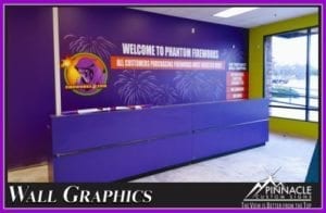 Vibrant lobby sign for Phantom Fireworks, designed by Pinnacle Custom Signs. The image features a large, colorful wall graphic behind the reception desk, welcoming visitors with the company logo and festive fireworks imagery, enhancing the interior atmosphere and brand identity.