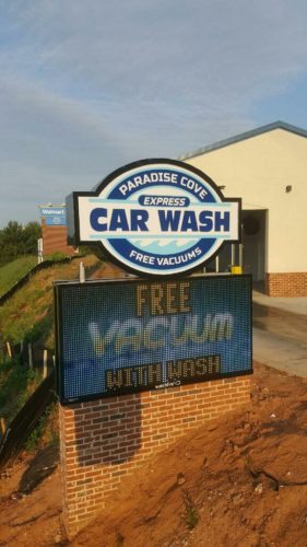 Outdoor sign for Paradise Cove Express Car Wash, designed by Pinnacle Custom Signs. The sign features a large logo with the text 'Car Wash' and 'Free Vacuums' along with a digital display screen that promotes 'Free Vacuum with Wash,' enhancing visibility and attracting customers.