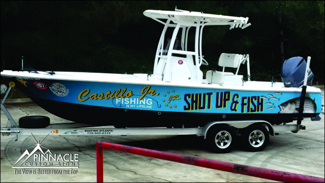 A boat on a trailer with a vibrant custom wrap that reads 'Castillo Jr. Fishing' and 'Shut Up & Fish' along the side. The wrap features bold lettering and fishing-themed graphics, showcasing the design and application expertise of Pinnacle Custom Signs.